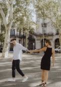 Playful couple walking through a tree-lined Barcelona square during a lifestyle session