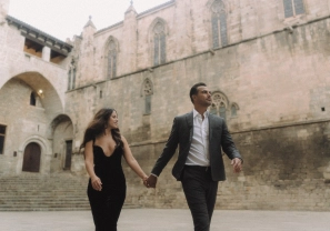 Elegant couple walking hand in hand across Plaça del Rei in Barcelona’s Gothic Quarter