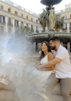 Couple laughing by the fountain at Plaça Reial in Barcelona with creative prism flare during a couples photoshoot