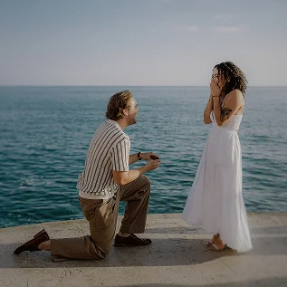 Surprise proposal by the sea in Barcelona with man kneeling and woman reacting