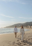 Couple walking along Barceloneta beach with footprints in the sand.