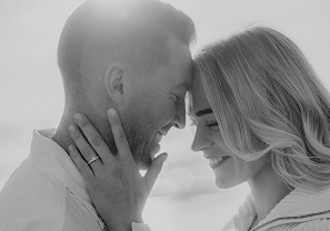Black-and-white close-up of forehead touch on the beach, engagement ring in focus