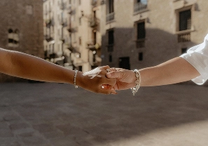 Two hands reaching together in a sunlit Gothic Quarter plaza, bracelets and ring detail