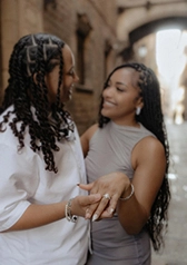 Just engaged couple smiling in an alley, hand forward showing the engagement ring