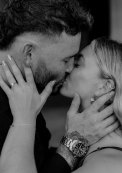 Close-up black and white portrait of a couple kissing, engagement ring visible on her hand