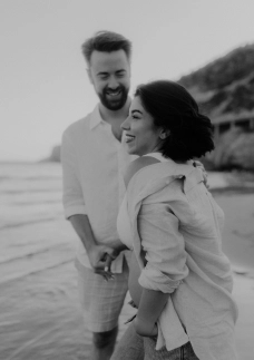 Black and white photo of a laughing couple walking together along Barcelona beach