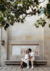 Expecting couple sitting on a stone bench surrounded by trees in Barcelona’s Gothic Quarter