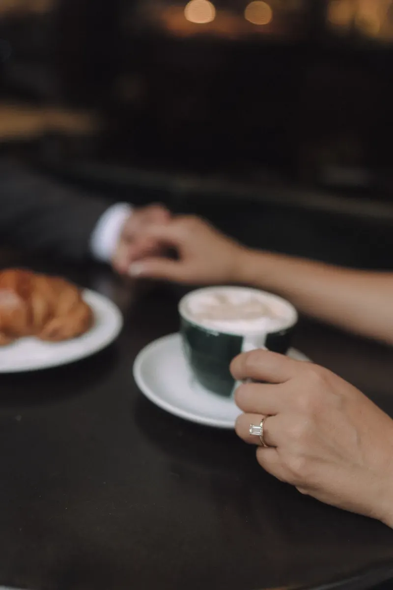 A close-up of Ashley and Edgar's hands beside coffee and breakfast at the cafe.