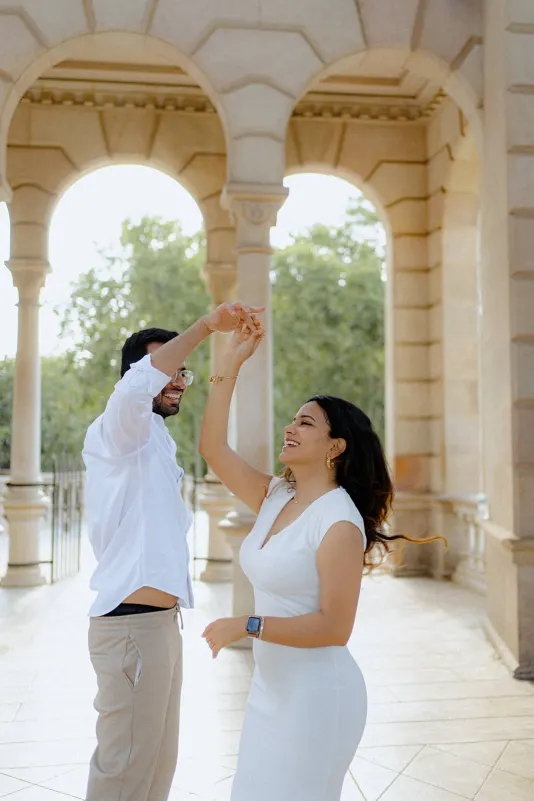 A couple dances and laughs together under sunlit arches during their surprise proposal photoshoot in Barcelona.