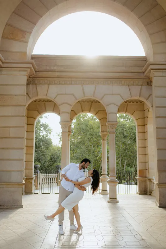 A couple dances and laughs under sunlit arches at Parc de la Ciutadella during their surprise proposal photoshoot.