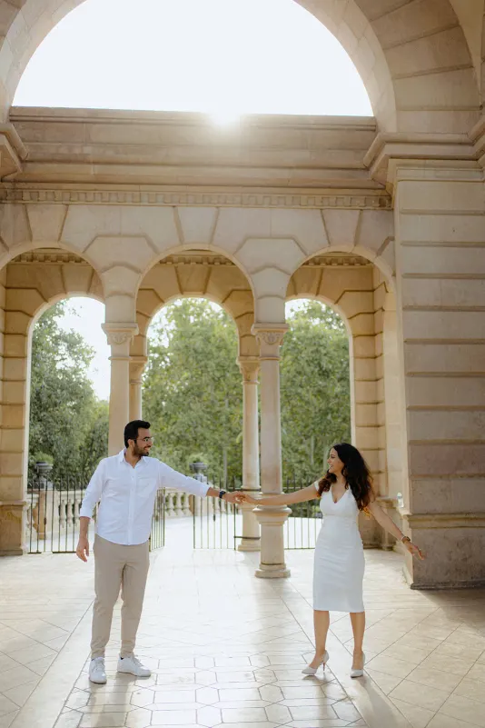 A couple dances joyfully beneath sunlit arches during their surprise proposal photoshoot at Parc de la Ciutadella.