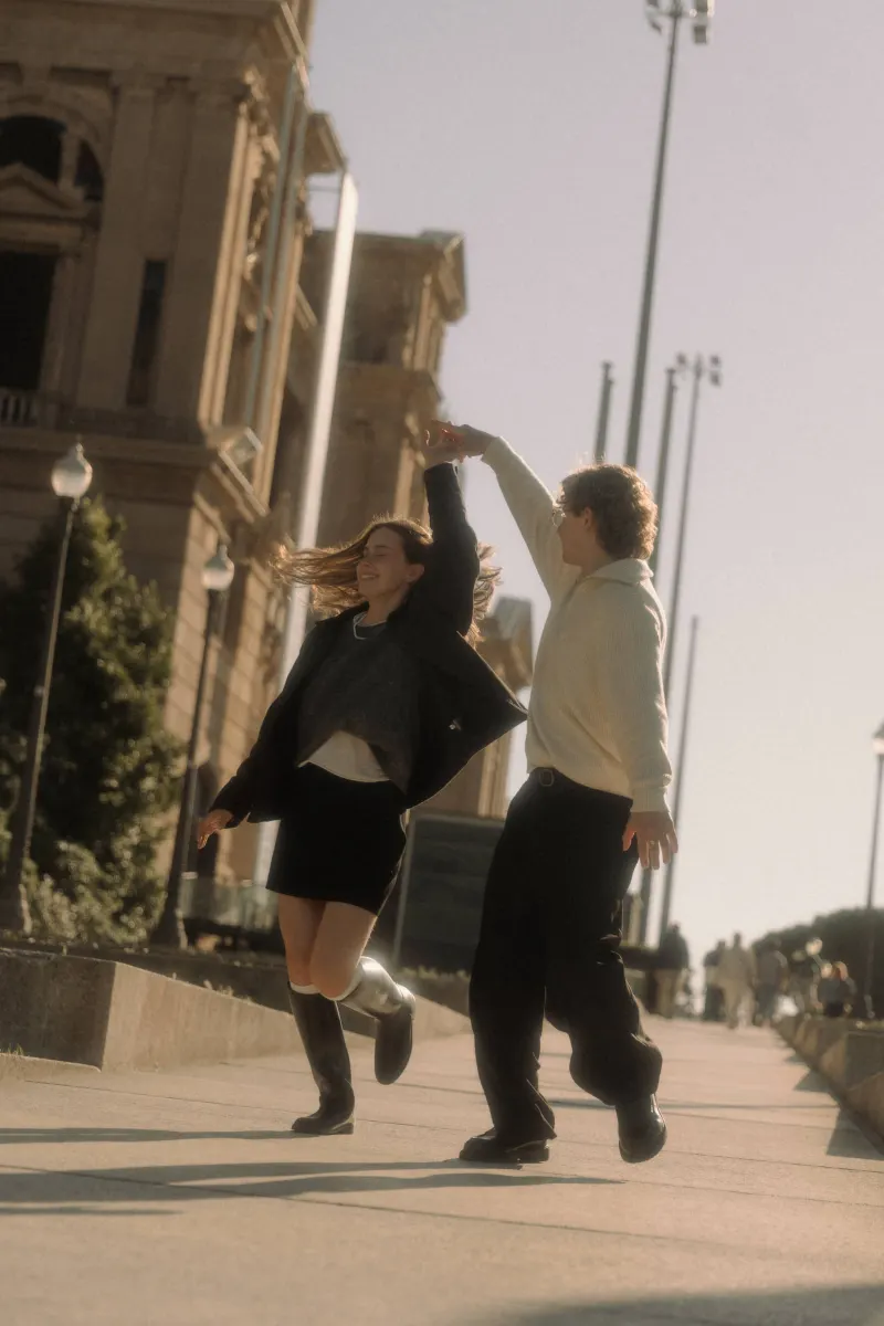 A couple dances playfully in the sunlight near historic architecture in Barcelona during a couples & engagements session.