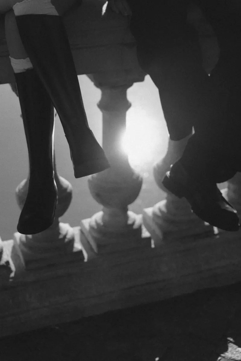 A couple dangles their feet over a sunlit stone railing, sharing a quiet moment during a Barcelona engagement session.