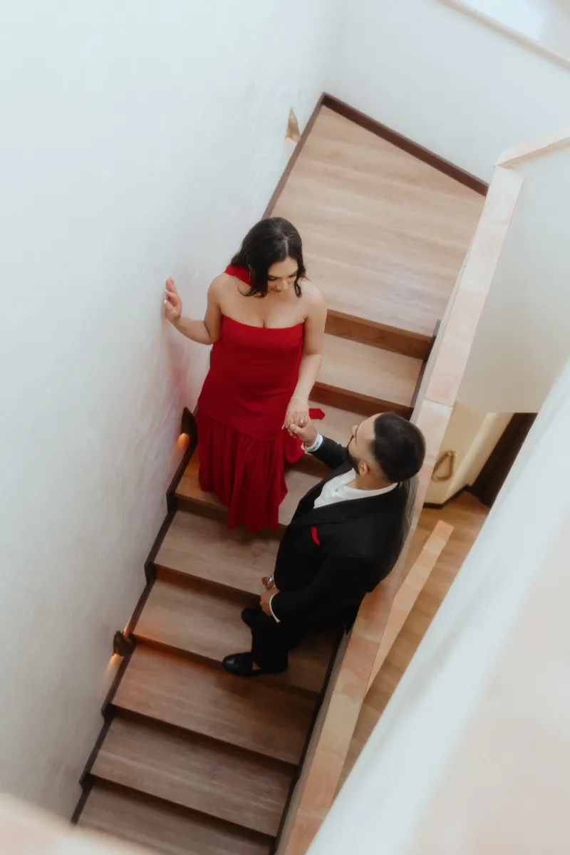 A couple dressed elegantly shares a quiet, intimate moment on a staircase during their surprise proposal photoshoot.
