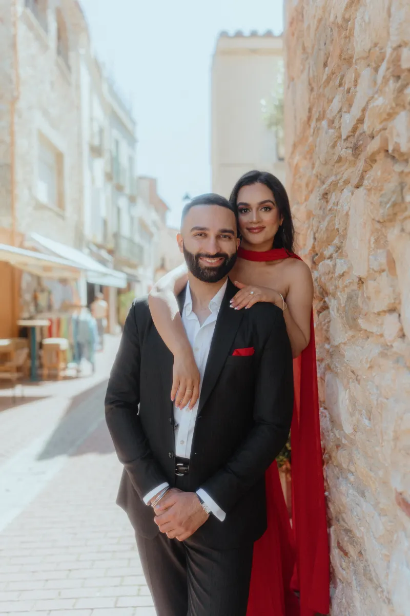 A couple dressed elegantly smiles together in a charming Begur alley during their surprise proposal photoshoot.