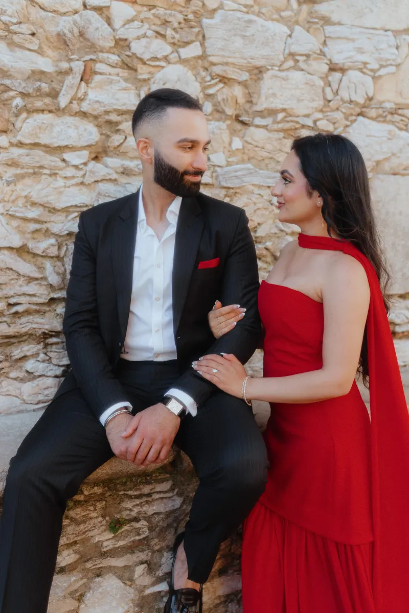 A couple dressed in formal attire share a loving gaze by a stone wall in Begur during a surprise proposal session.