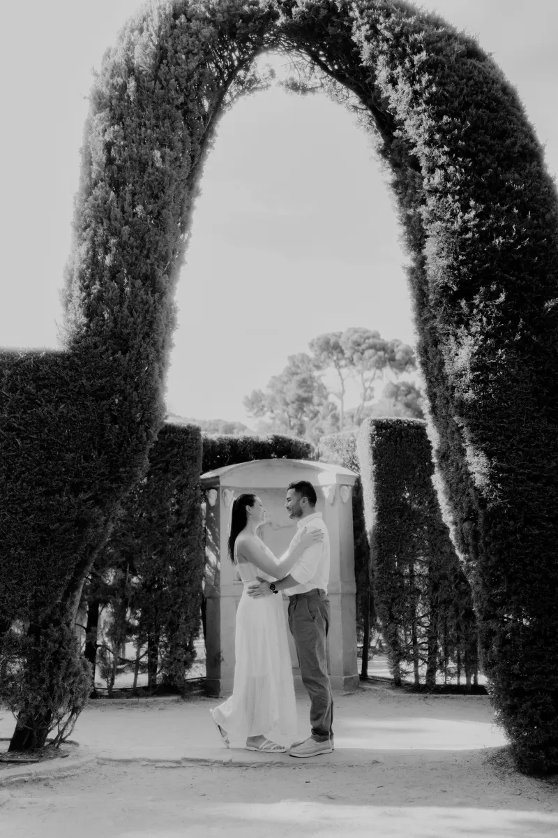 A couple embraces and laughs beneath a sculpted garden arch during a romantic couples & engagements session.