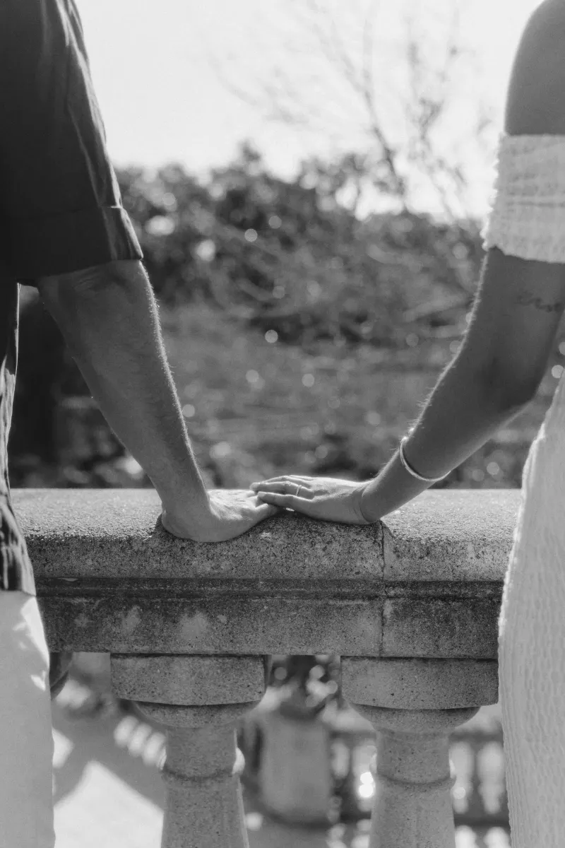 A couple gently touching hands on a stone railing, capturing a quiet, romantic moment from an engagement session.
