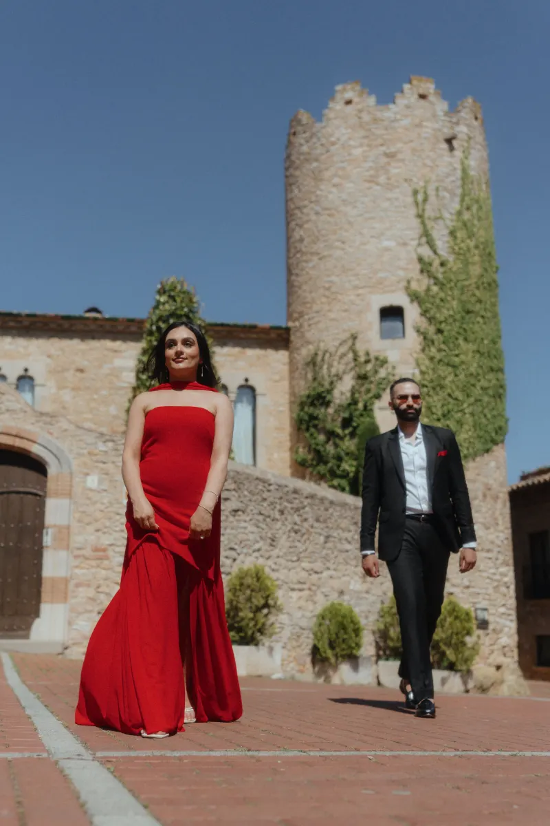 A couple in chic attire walks through Begur’s old town, capturing candid moments during their surprise proposal photoshoot.