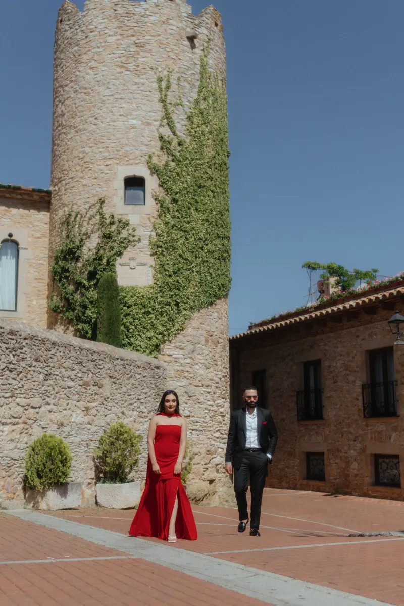 A couple in elegant attire strolls through Begur’s historic streets during their surprise proposal photoshoot.
