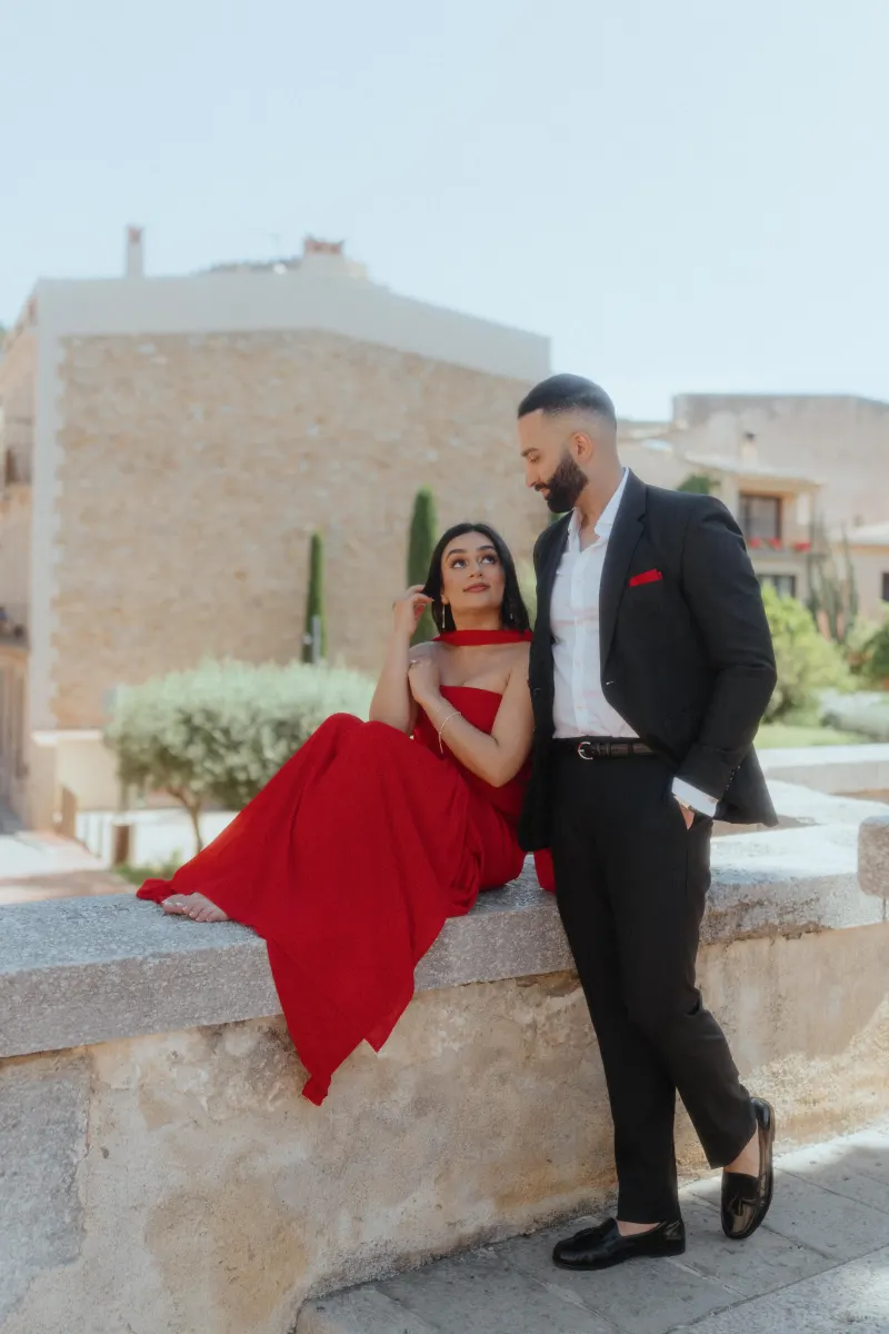 A couple in formal outfits share a romantic moment on a stone ledge in Begur during their surprise proposal photoshoot.