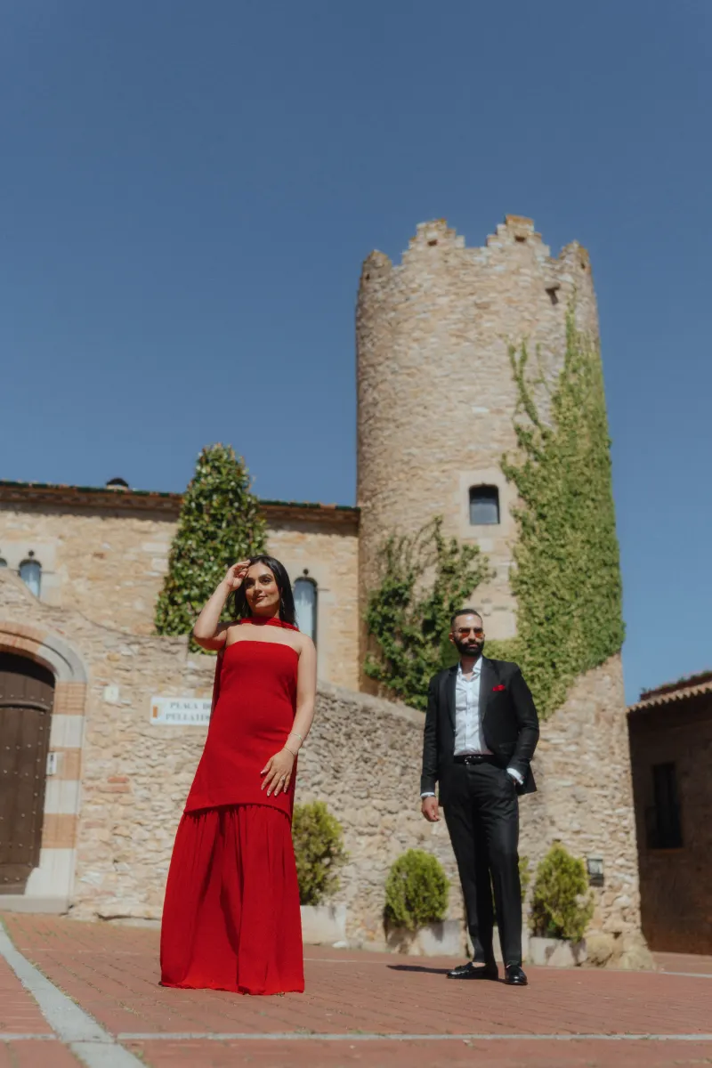 A couple in formal outfits stands confidently in Begur’s old town during their surprise proposal photoshoot.
