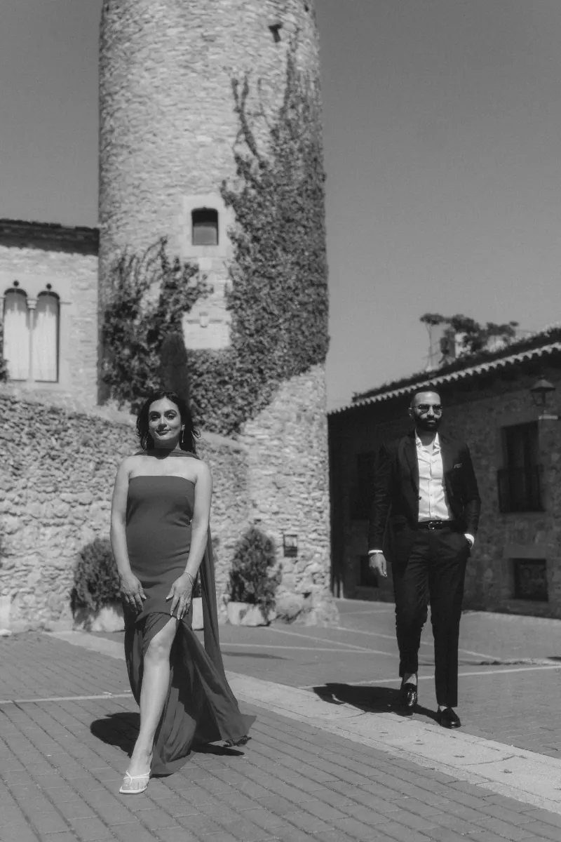 A couple in formal wear shares a joyful moment in Begur’s old town during their surprise proposal photoshoot.