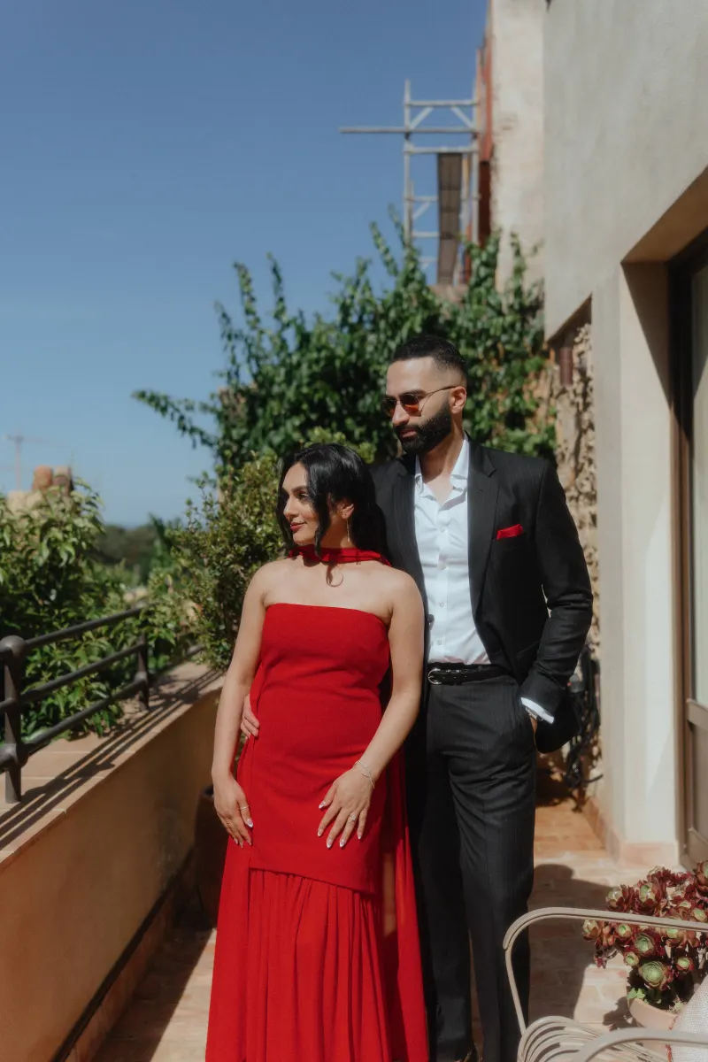 A couple in stylish outfits enjoys a quiet, sunlit moment on a terrace during their surprise proposal photoshoot.