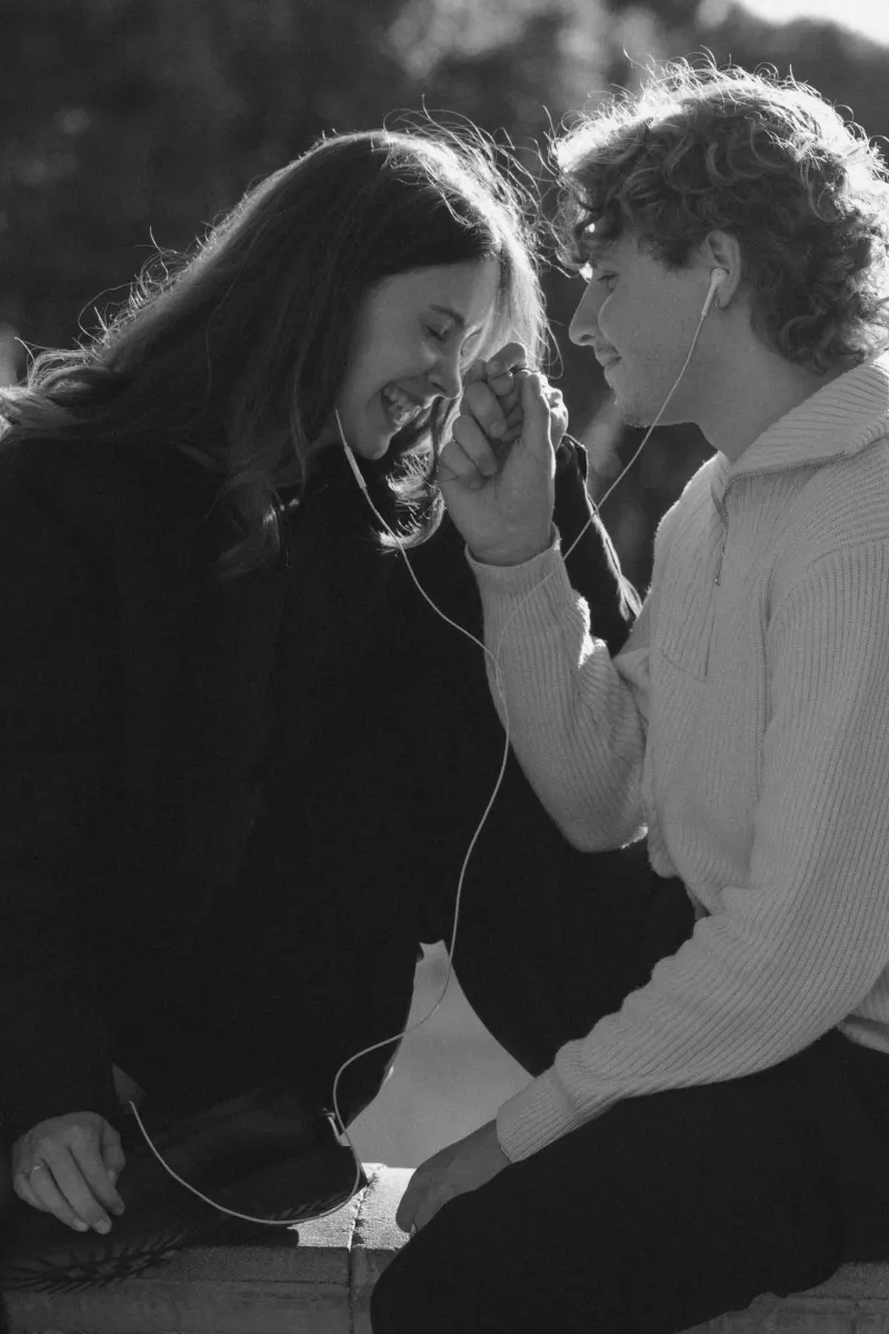 A couple laughs and holds hands while sharing headphones, captured during a candid couples & engagements photoshoot in Barcel