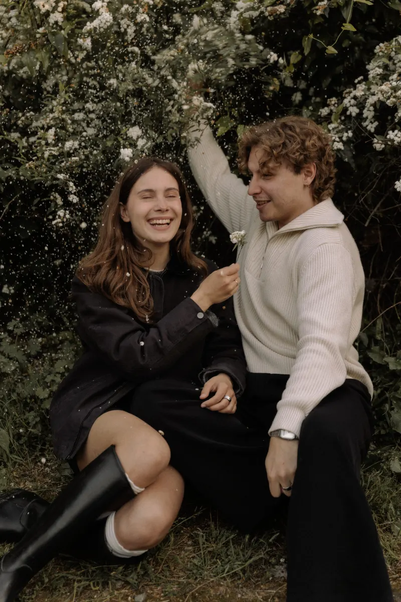 A couple laughs together as flower petals fall around them during a playful couples & engagements photoshoot in Barcelona.