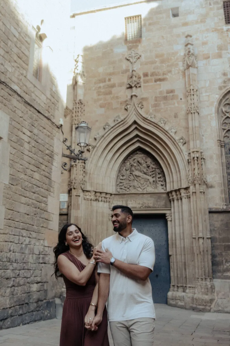 A couple laughs together, holding hands during a couples & engagements photoshoot in a historic stone courtyard.