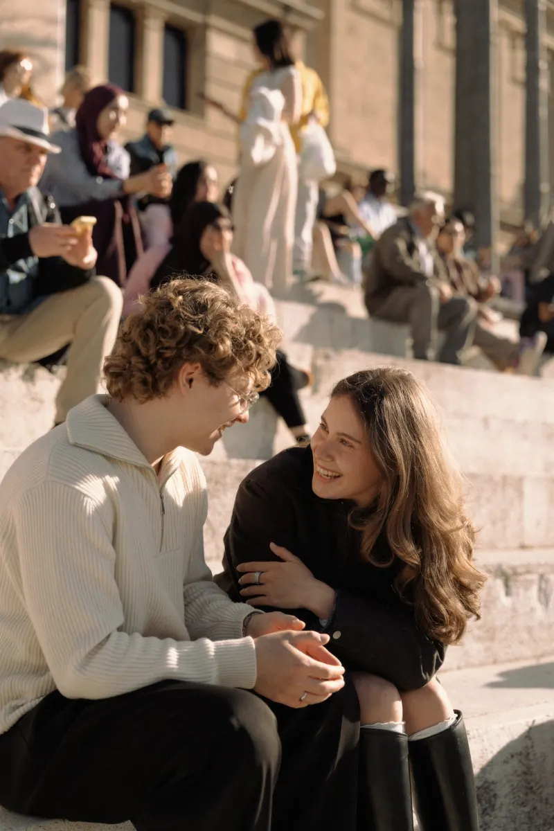 A couple laughs together on sunlit stone steps in Barcelona, captured during a candid couples & engagements session.