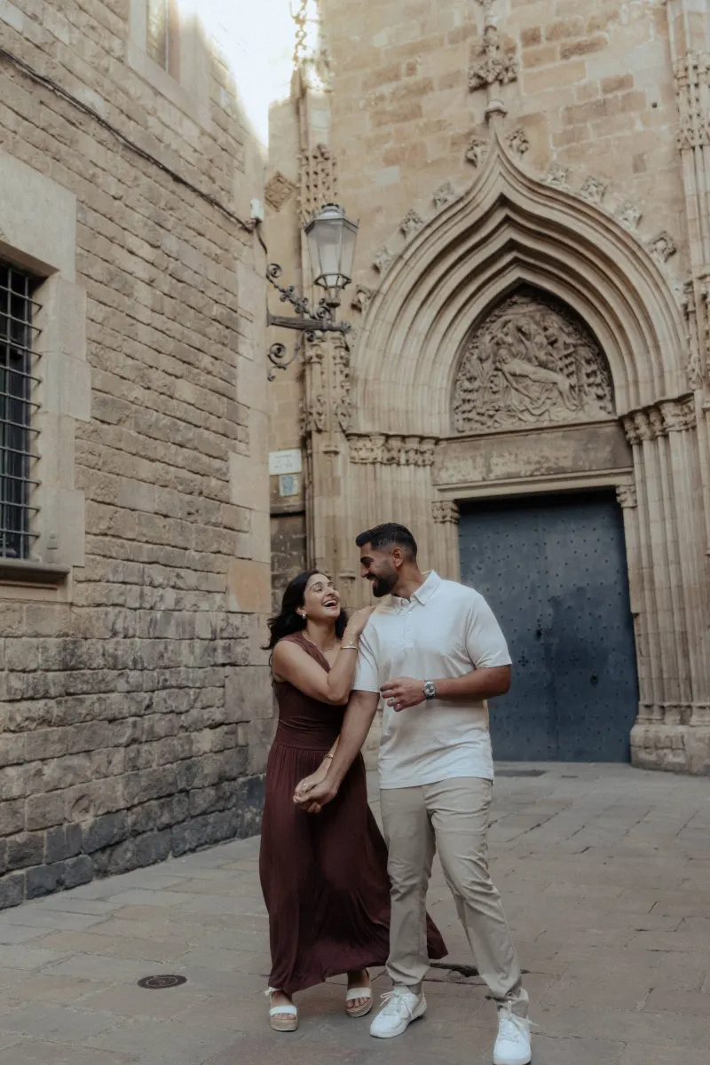A couple laughs together while strolling past a gothic doorway during their couples & engagements photoshoot.