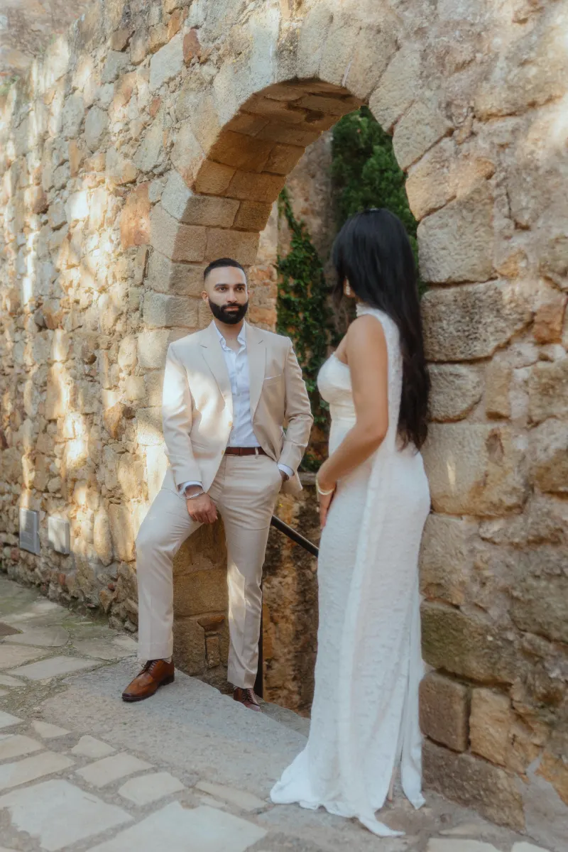 A couple pauses for a candid moment by a rustic stone archway during their surprise proposal photoshoot.