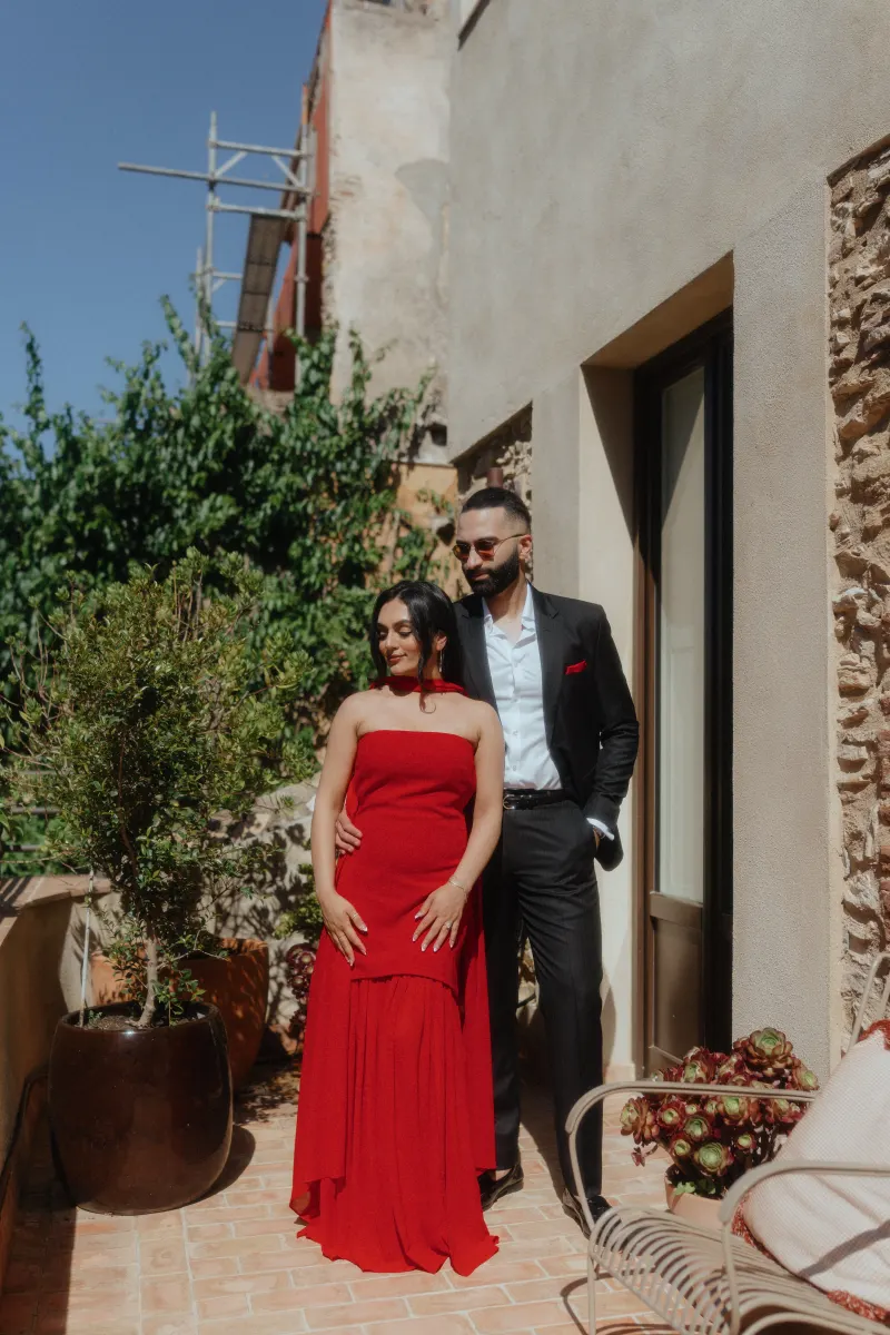 A couple poses in elegant attire on a sunlit terrace, captured during their surprise proposal photoshoot.