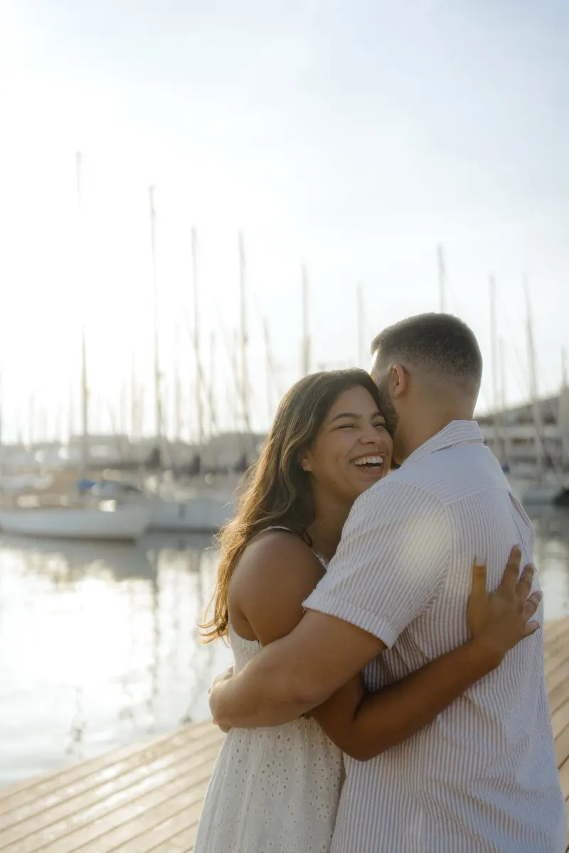 A couple shares a joyful embrace on a marina dock, captured during an engagement photoshoot at sunset.