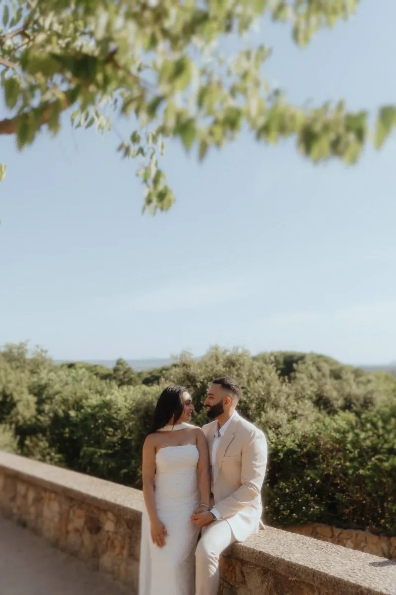 A couple shares a joyful, intimate moment on a sunlit stone wall after their surprise proposal photoshoot.