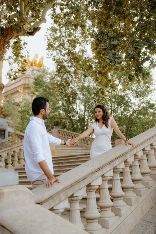 A couple shares a joyful moment holding hands on the grand staircase during a surprise proposal photoshoot in Barcelona.