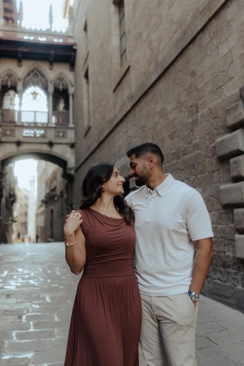 A couple shares a loving smile, arm in arm, during their engagement photoshoot in a historic European alleyway.