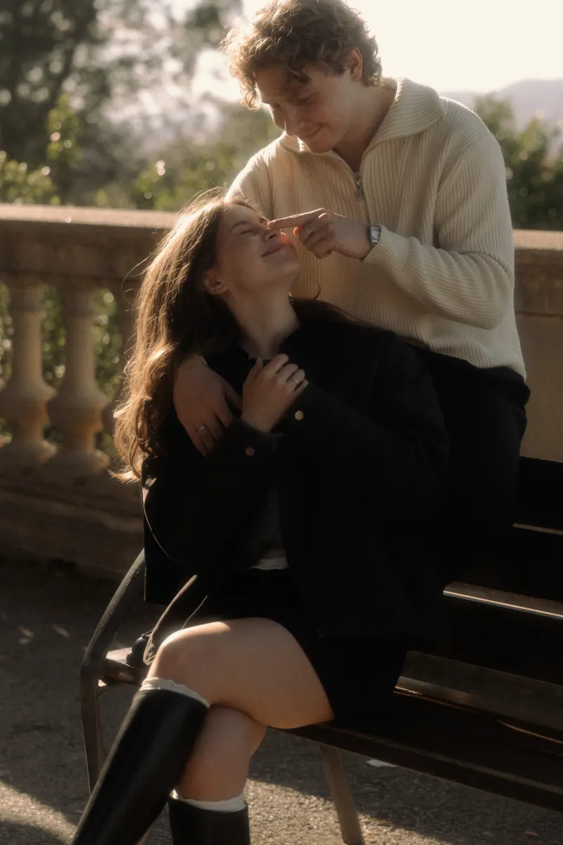 A couple shares a playful, affectionate moment on a sunlit bench in Barcelona during a couples & engagements shoot.