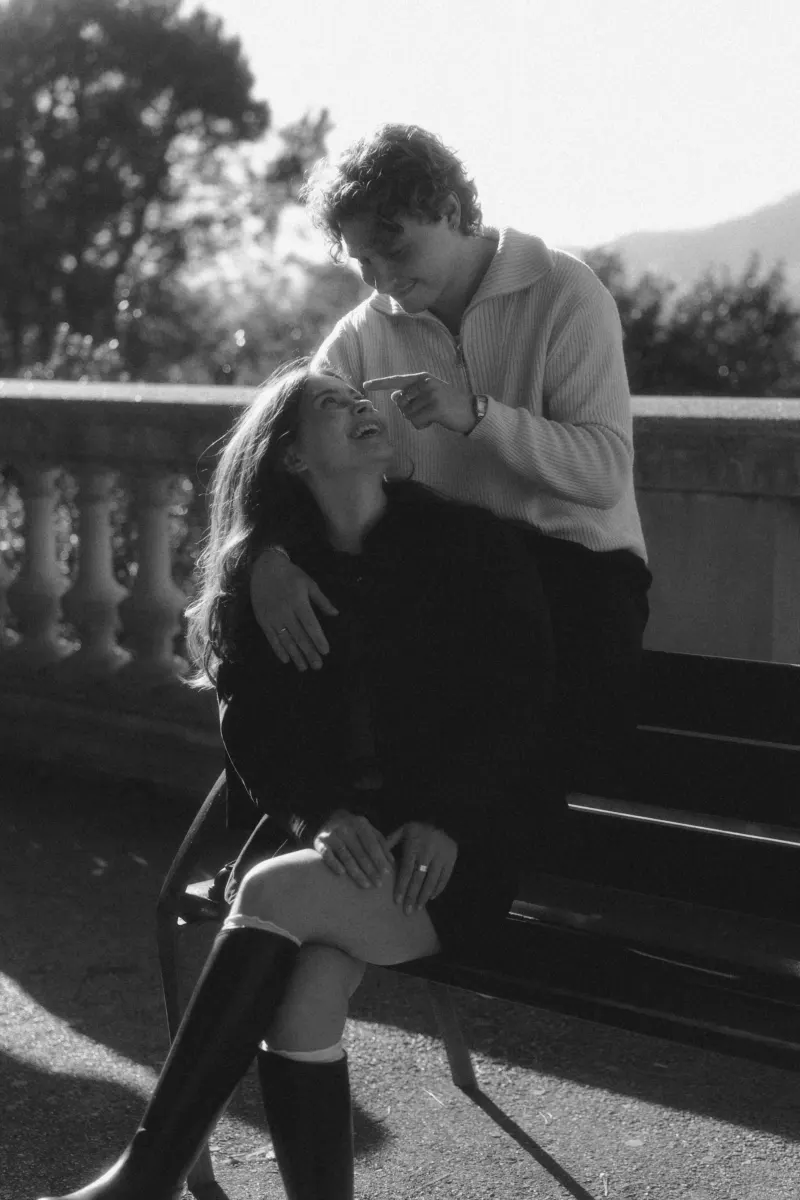 A couple shares a playful, affectionate moment on a sunlit bench in Barcelona during an engagement photoshoot.