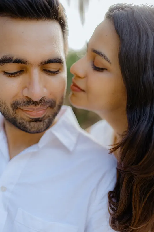 A couple shares a quiet, affectionate moment during their surprise proposal photoshoot, both smiling softly in the sunlight.