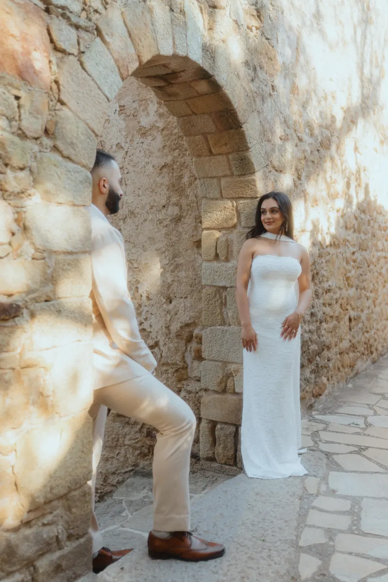 A couple shares a quiet, loving look under a sunlit stone archway during their surprise proposal photoshoot.