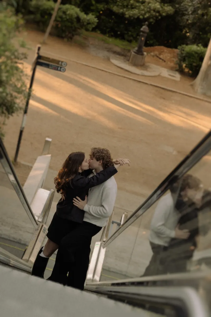 A couple shares a romantic kiss on an outdoor escalator in Barcelona during a couples & engagements photoshoot.