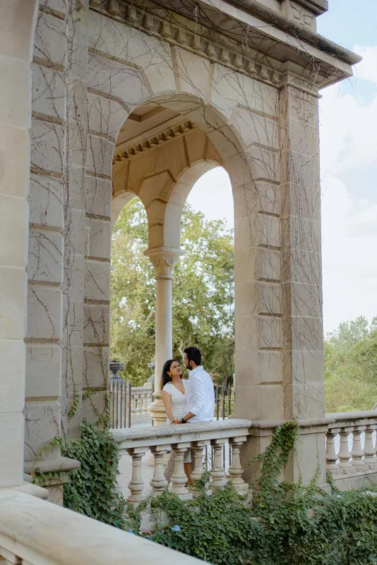 A couple shares a romantic moment on a vine-covered terrace during their surprise proposal photoshoot in Parc de la Ciutadell