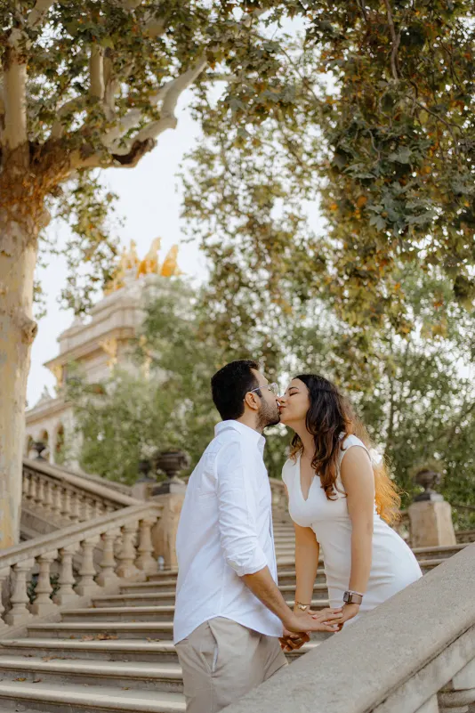 A couple shares a sweet kiss on the steps at Parc de la Ciutadella during their surprise proposal photoshoot.