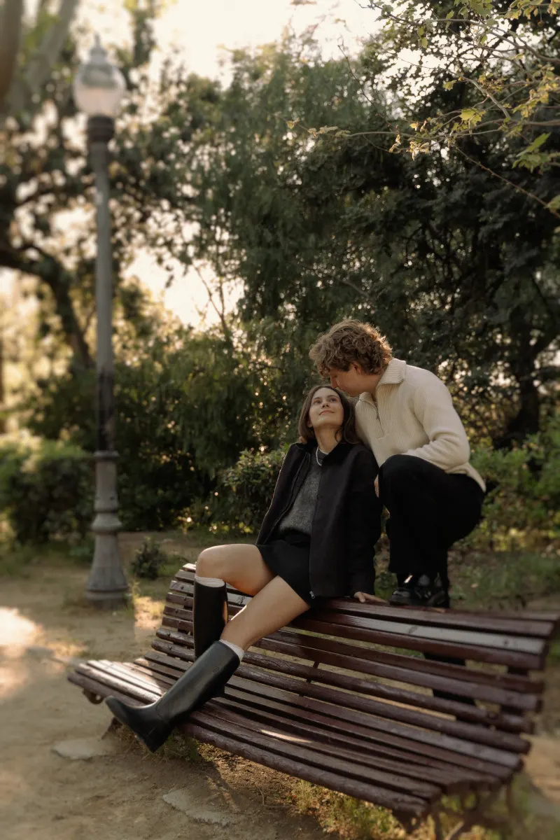 A couple shares a sweet moment on a park bench in Barcelona during a relaxed couples & engagements photoshoot.