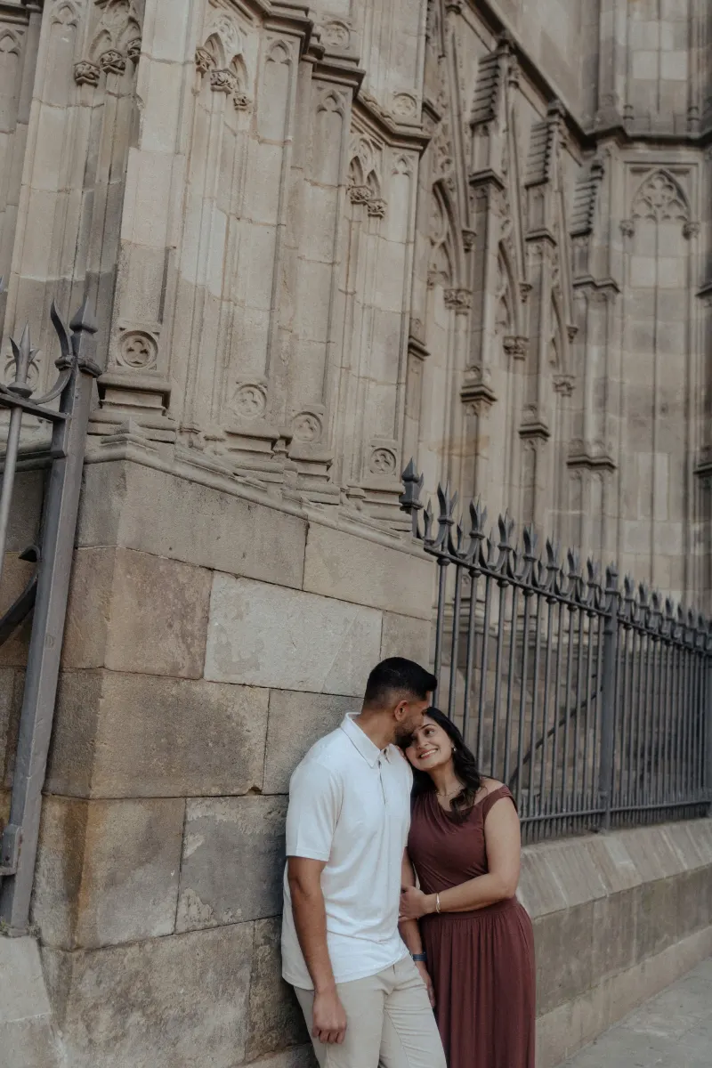 A couple shares a tender embrace by a historic stone building during their engagement photoshoot.