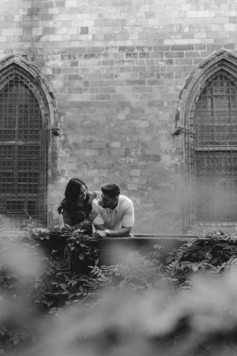 A couple shares a warm laugh together by ivy-covered stonework during a couples & engagements photoshoot in a historic courty
