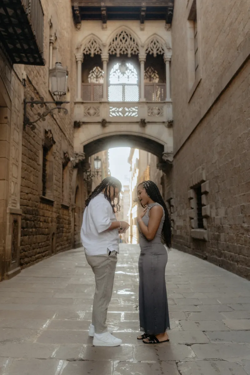 A couple shares an emotional proposal moment beneath Barcelona’s Gothic bridge during a surprise proposal photoshoot.